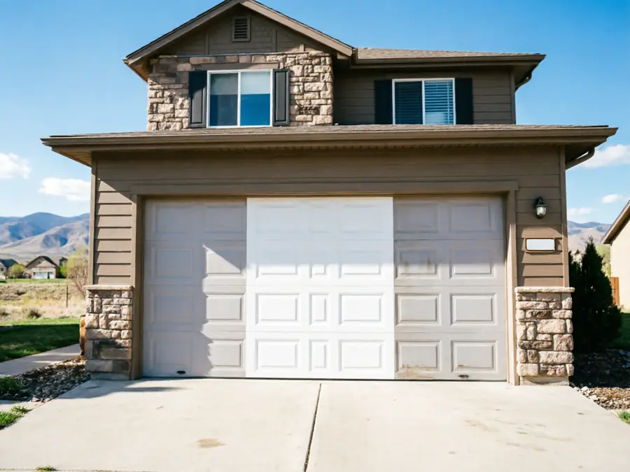 The garage door is half clean and half dirty, with a house and mountains behind it.